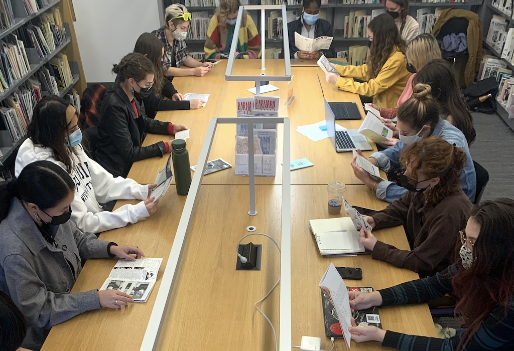 photo of masked students at a table reading zines, zine shelves in the background