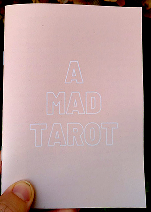 photo of a zine cover: little thumb on the bottom left holding the zine, which is pink with the title in white outline letters