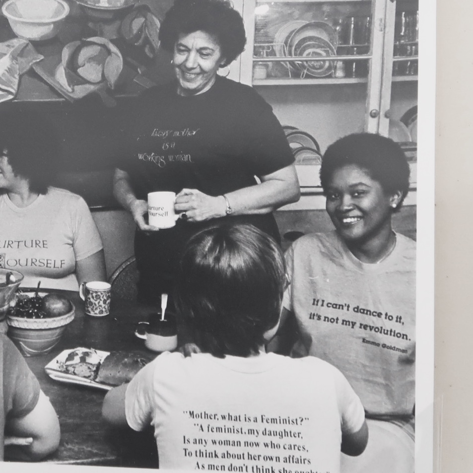 photograph of women gathered around table wearing feminist slogan shirts