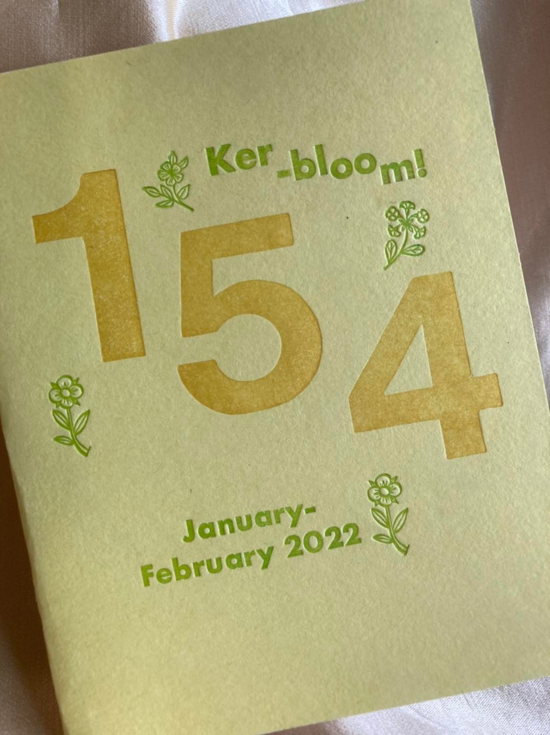 photo of zine: light yellow cardstock background, letterpress title in green around a giant "154" in gold