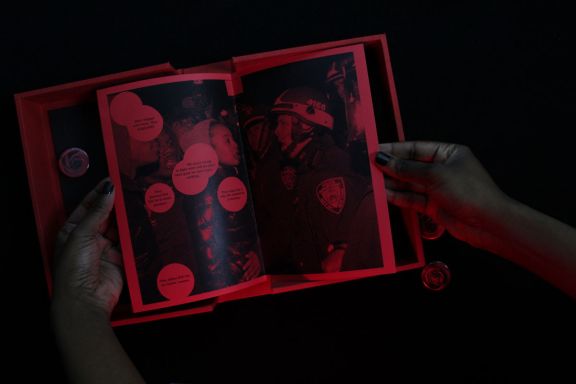 photo of a Black woman's hands holding open a red zine to a page with citizens and police and  speech bubbles