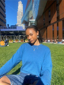 photo of Zoë sitting on the Barnard campus, with the Diana Center in the background