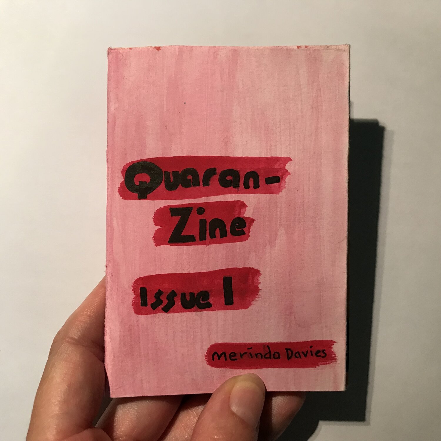photo of hand holding zine: red title on pink background