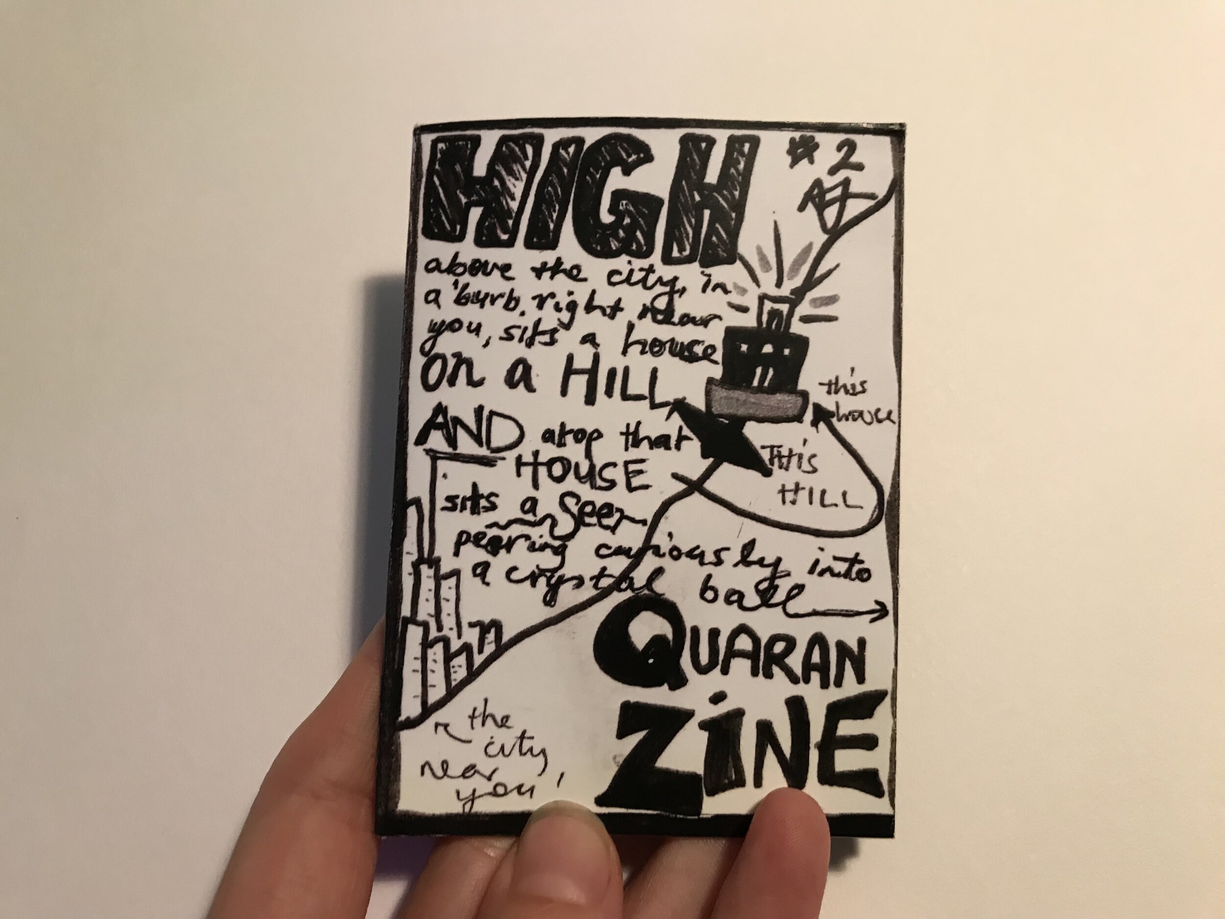 photo of fingers holding black and white zine: mostly text, also drawing of a building on a hill